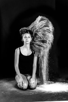 Vrouw op haar knieën in een wolk poeder, lang haar opzij uitgeslagen, zwart-wit