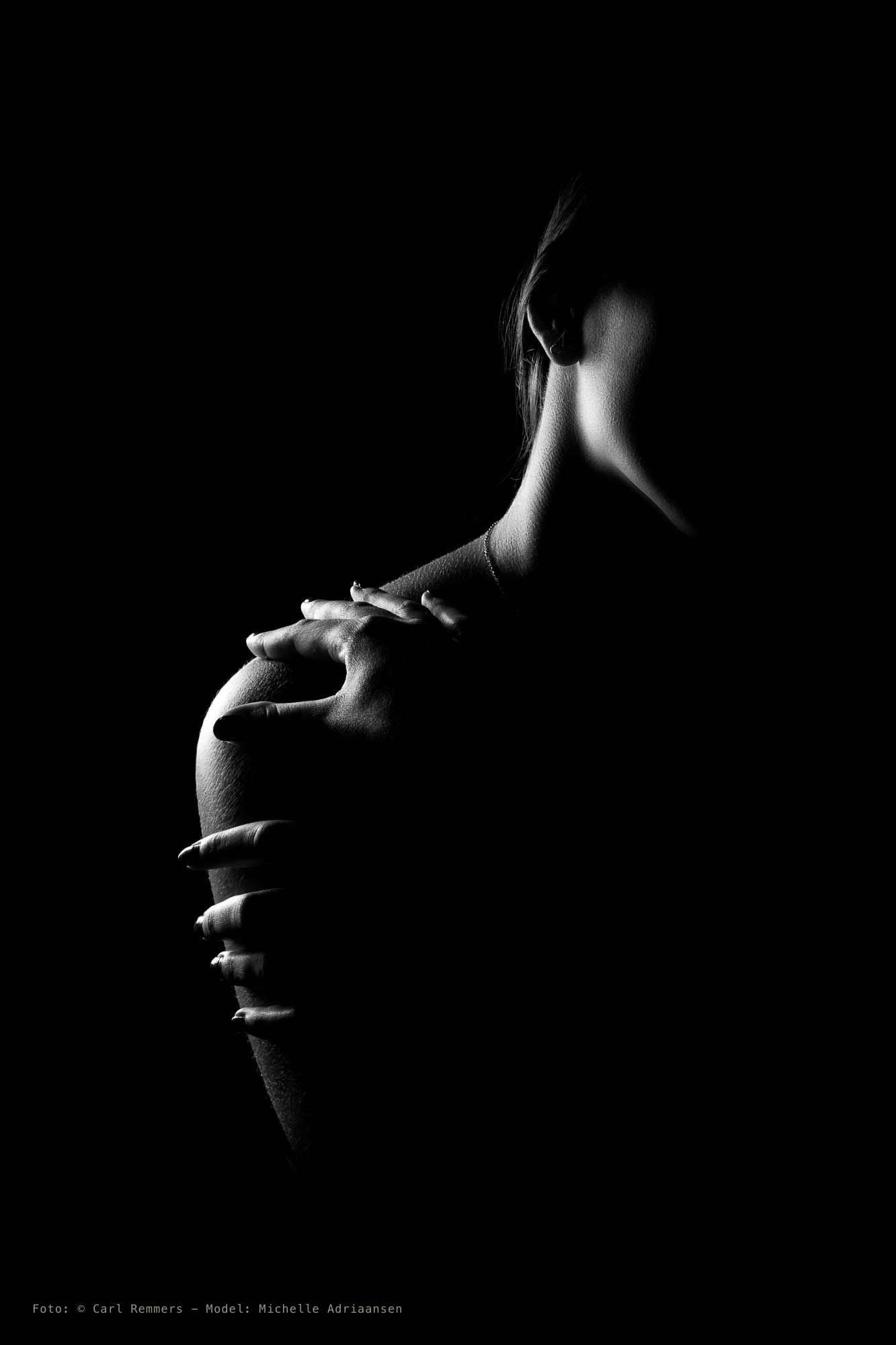 Silhouette of a neck and shoulder in raking light, a hand on the shoulder, black and white