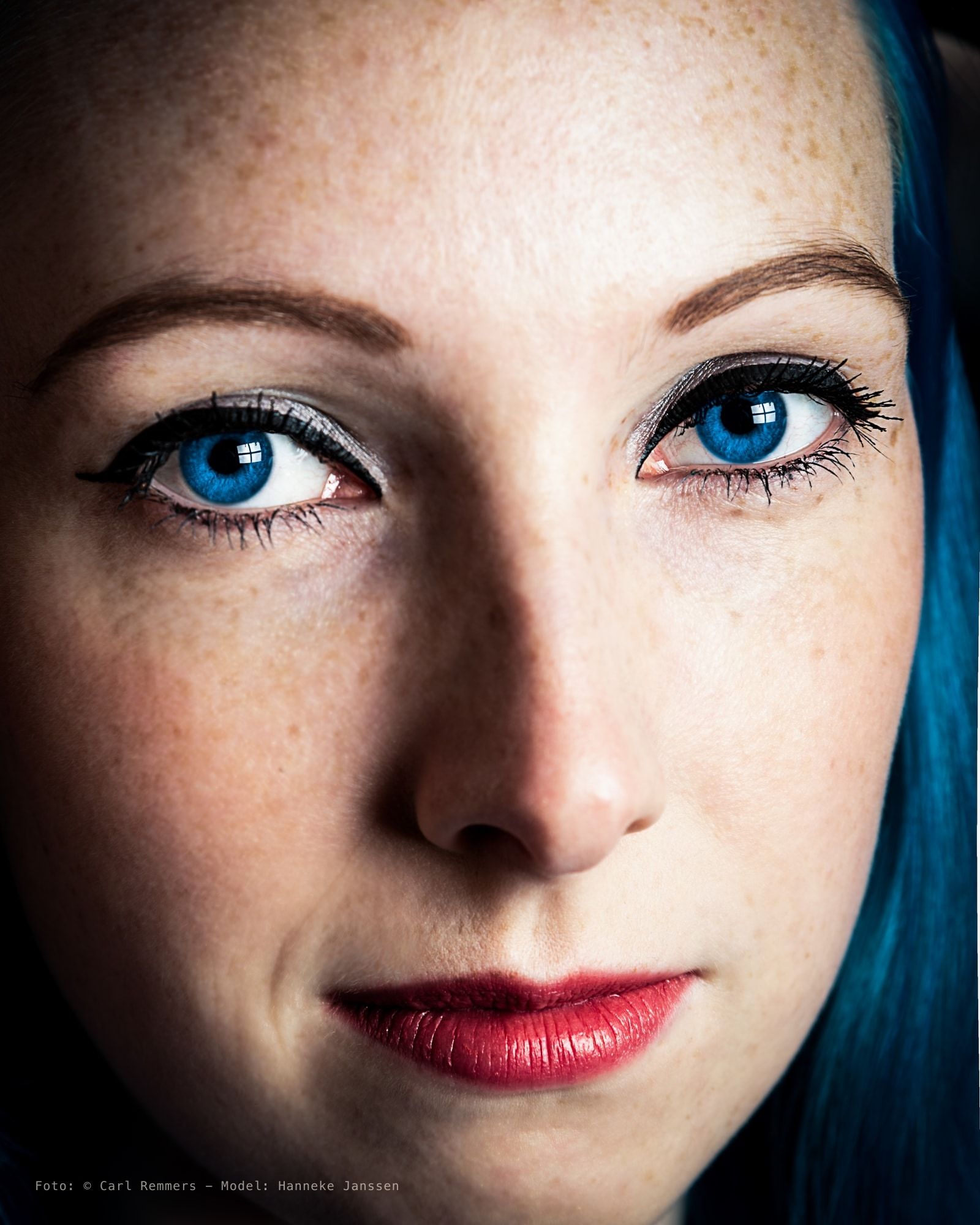 Close-up van een gezicht met blauwe ogen, sproeten, rode lippen en blauw haar
