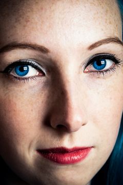 Close-up van een gezicht met blauwe ogen, sproeten, rode lippen en blauw haar