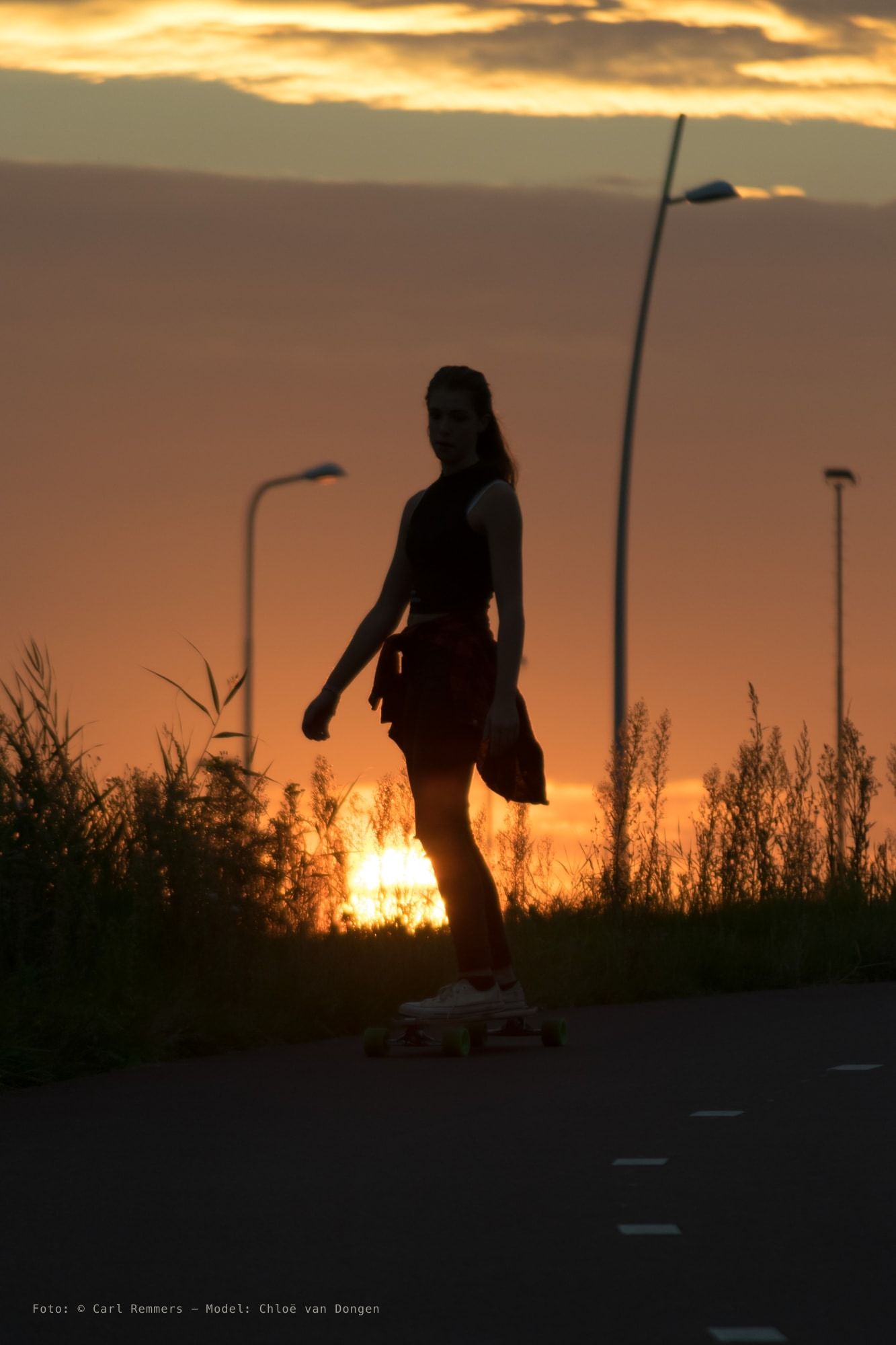 Silhouet van een vrouw op een longboard tegen een oranje avondlucht