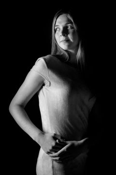 Vrouw in een lichte jurk met haar handen voor zich, half in het donker, zwart-wit