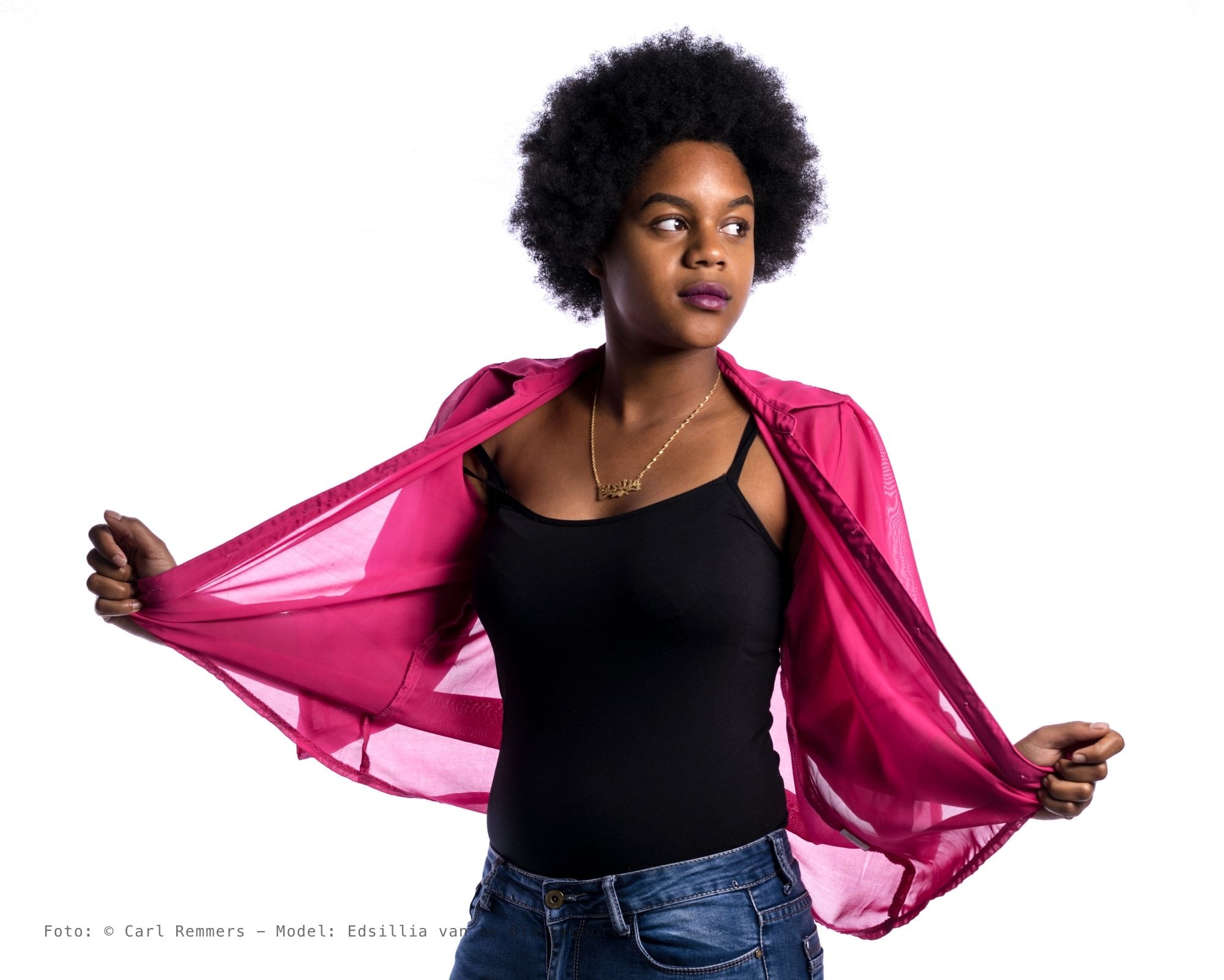 Vrouw met afrokapsel trekt een roze blouse open over een zwart hemd, witte achtergrond