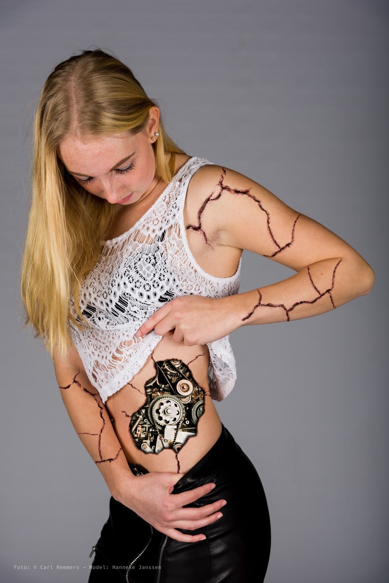 Vrouw met bodypaint van barsten en tandwielen op haar buik, witte kanten top