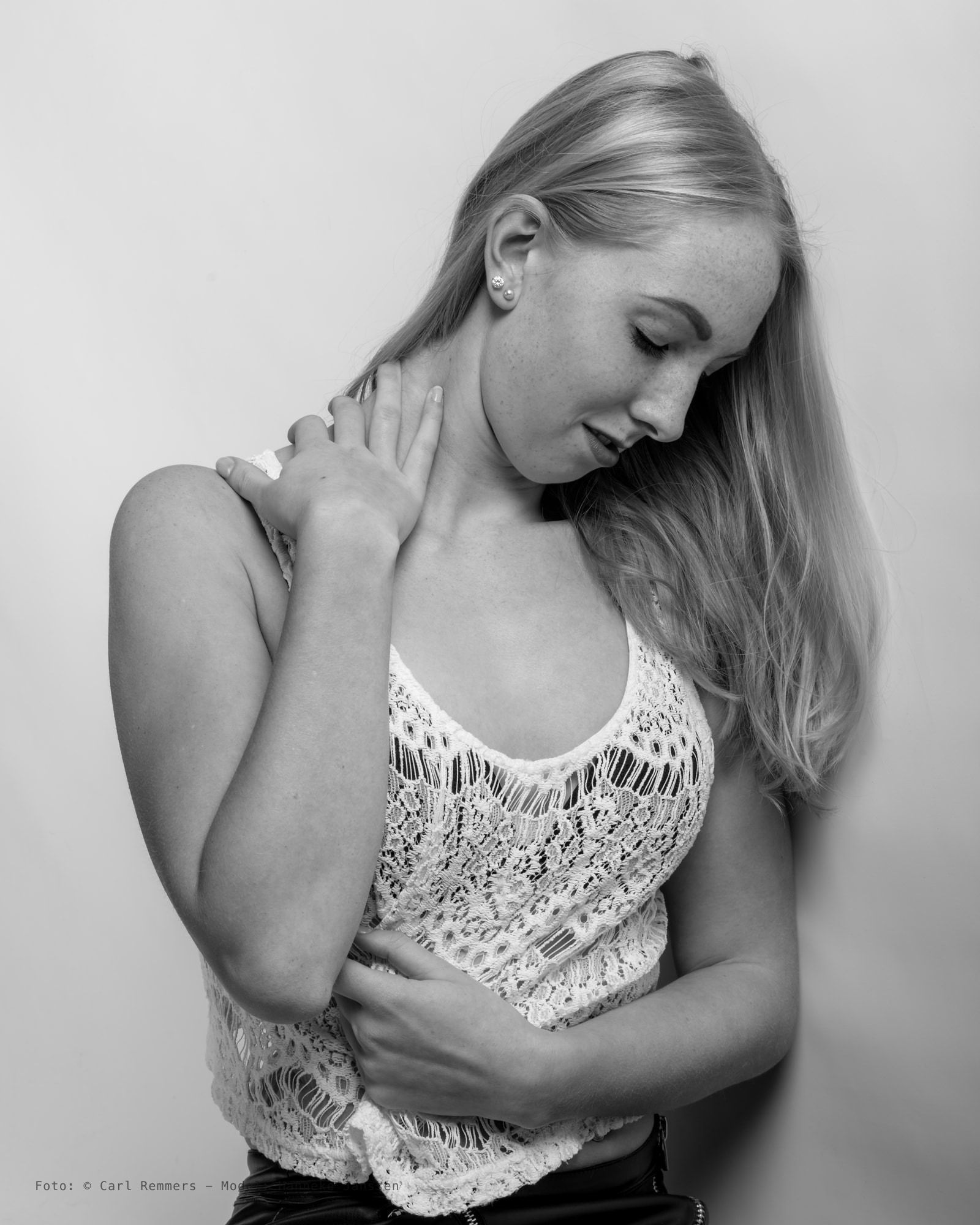 Vrouw met blond haar in een witte kanten top, een hand op haar schouder, zwart-wit