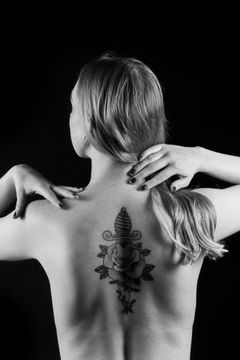 Naaktstudie van een rug met een tatoeage van een dolk door een roos, handen in de nek, zwart-wit