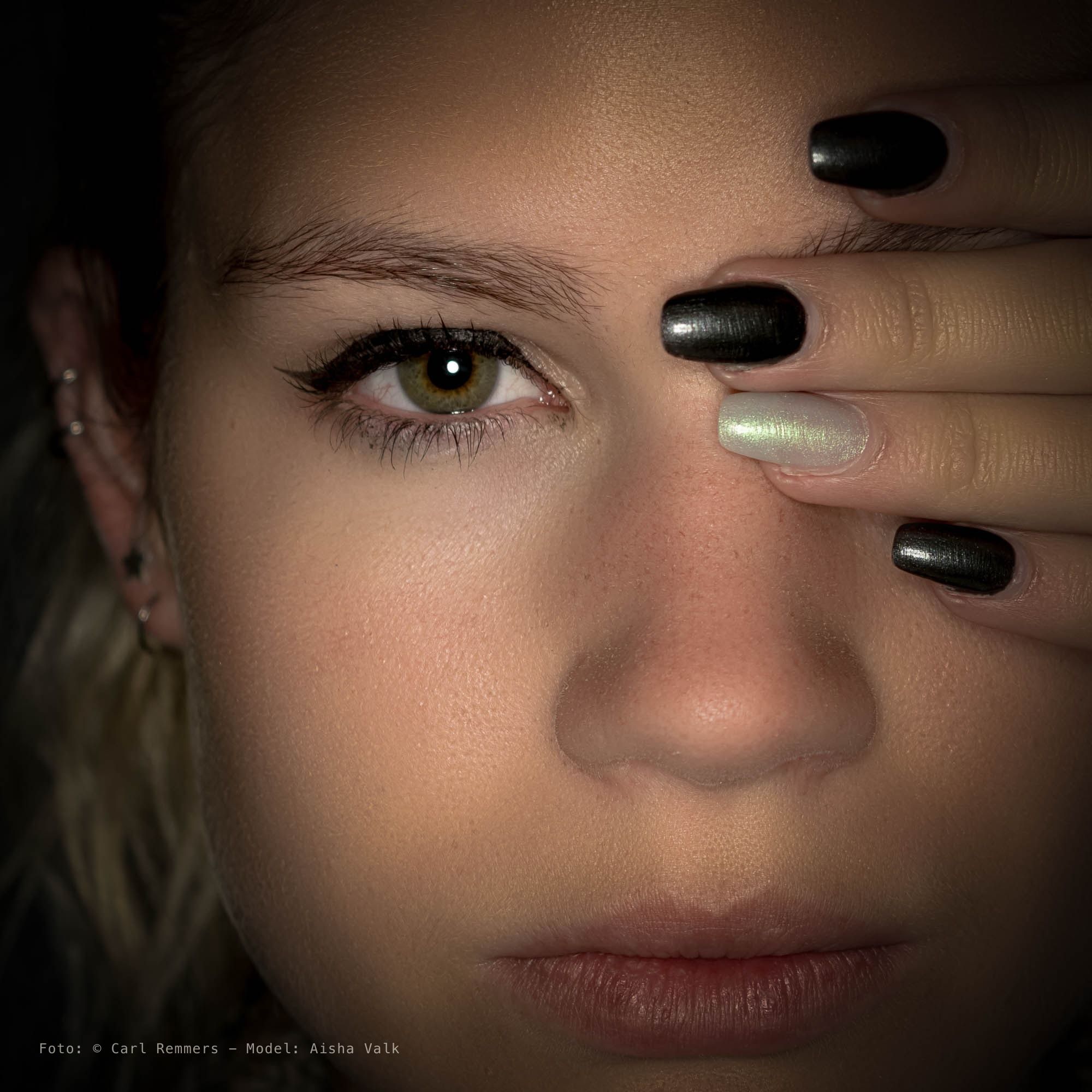 Close-up van een oog, een hand met zwartgelakte nagels langs het gezicht