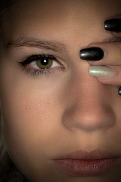 Close-up van een oog, een hand met zwartgelakte nagels langs het gezicht