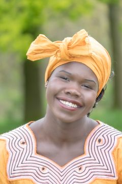 Lachende vrouw met een oranje hoofddoek, buiten tussen groene bomen