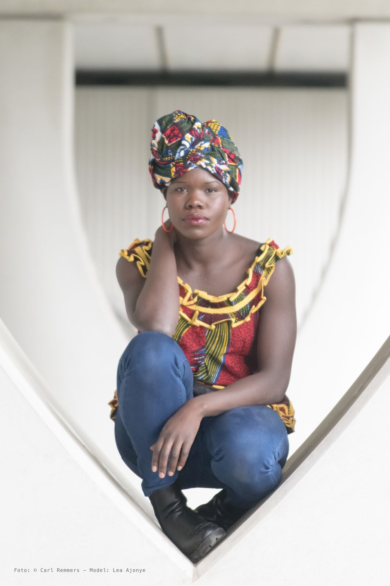 Woman with a flowered headscarf and large hoop earrings crouching in a white alcove