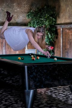 Vrouw zweeft horizontaal boven een pooltafel en stoot, levitatiefoto