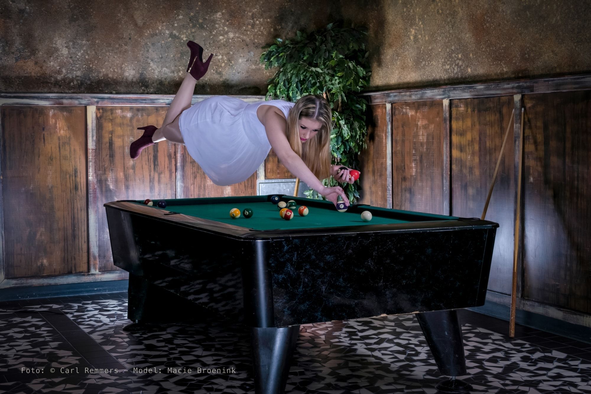 Vrouw zweeft horizontaal boven een pooltafel en stoot, levitatiefoto