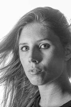 Vrouw met waaiend haar tegen een witte achtergrond, zwart-wit