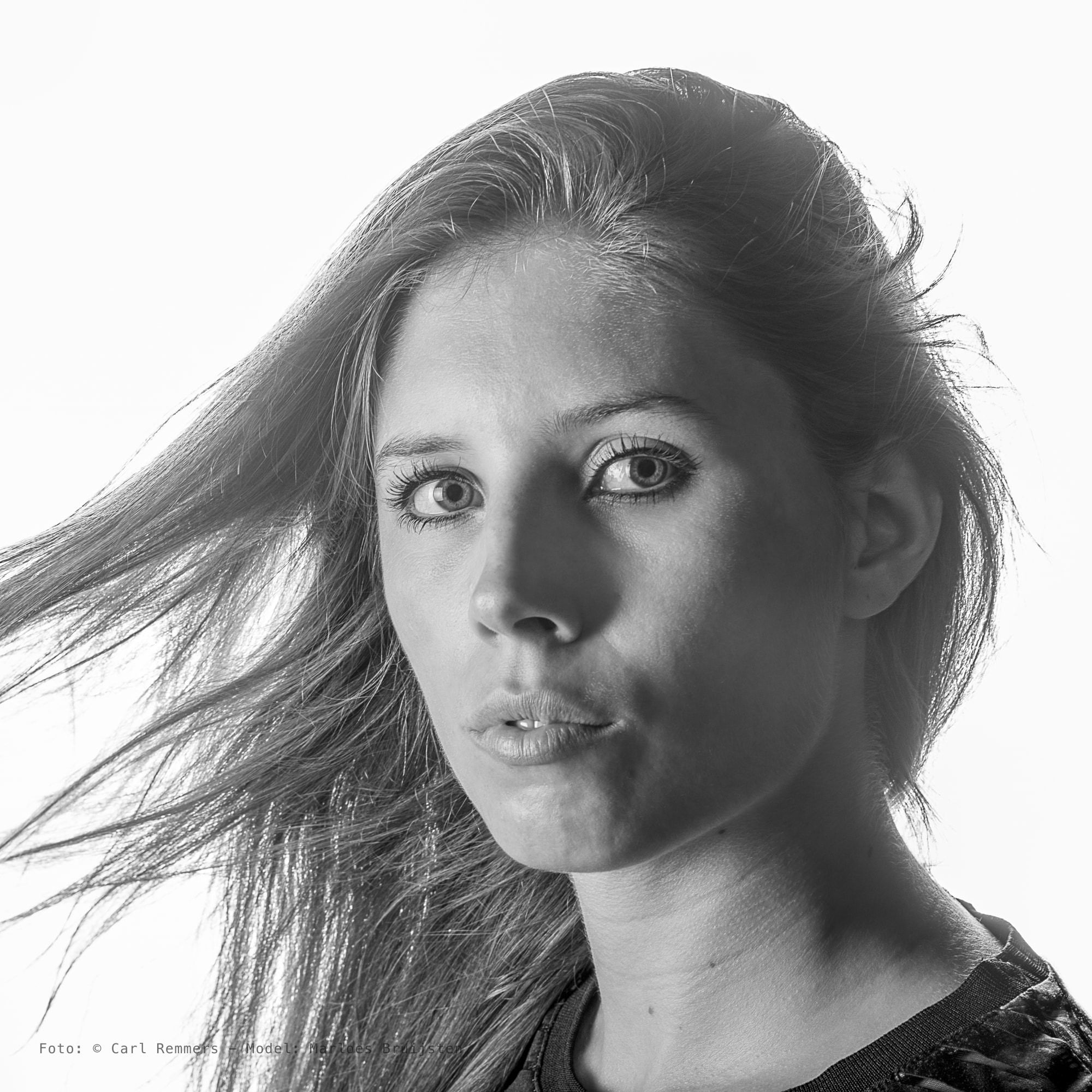 Vrouw met waaiend haar tegen een witte achtergrond, zwart-wit