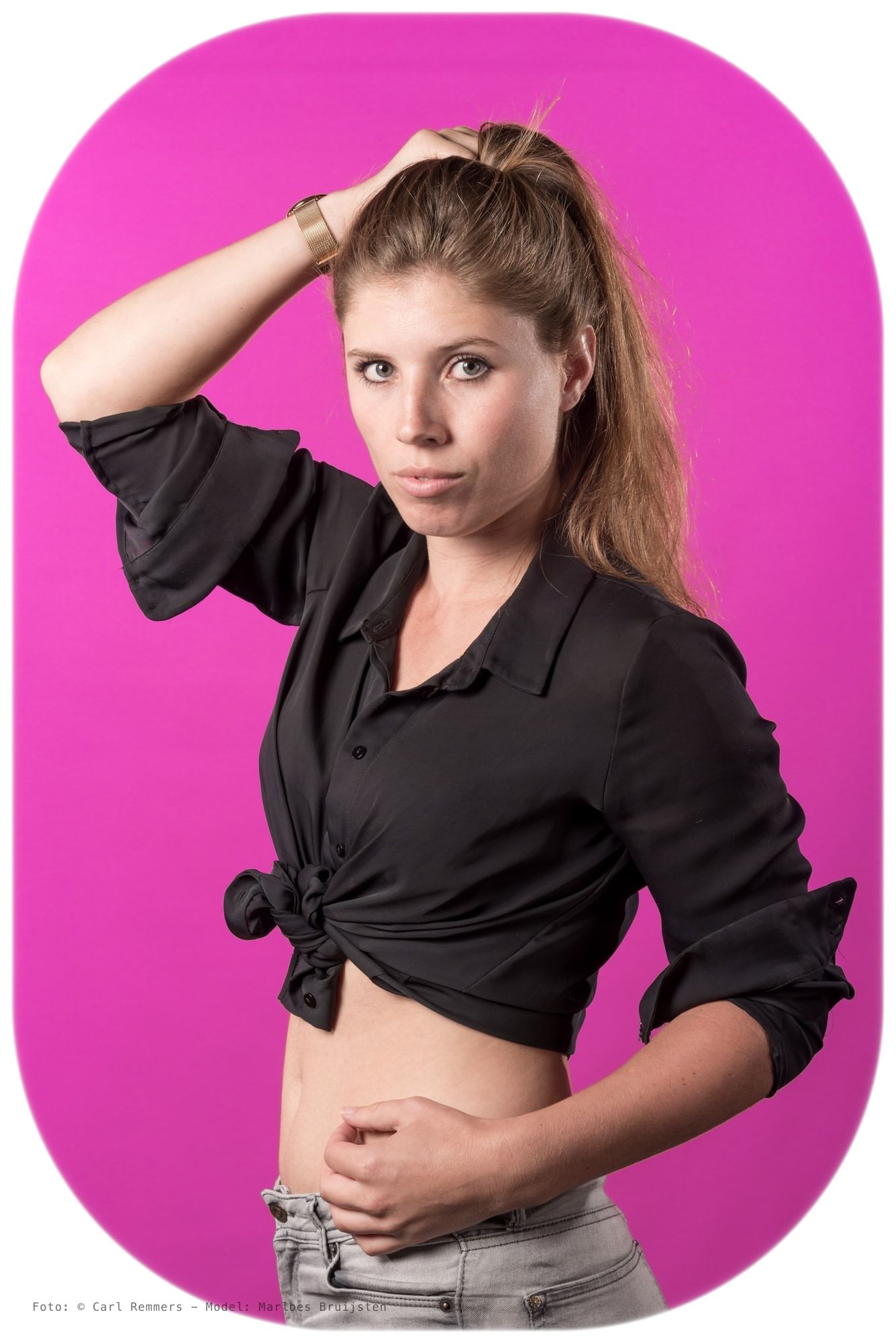 Woman in a knotted black shirt, hand in her hair, bright pink background