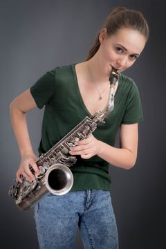 Vrouw met een saxofoon aan haar mond, groen T-shirt, grijze achtergrond