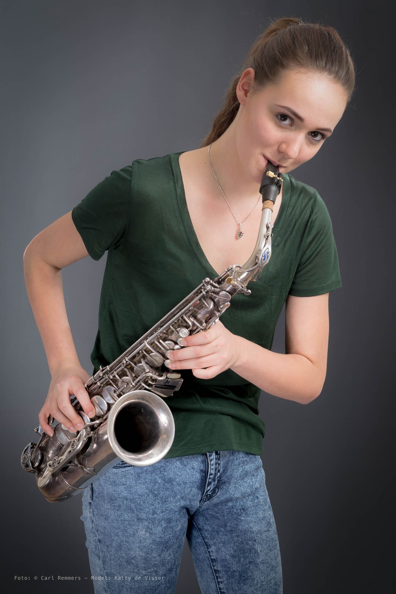 Vrouw met een saxofoon aan haar mond, groen T-shirt, grijze achtergrond