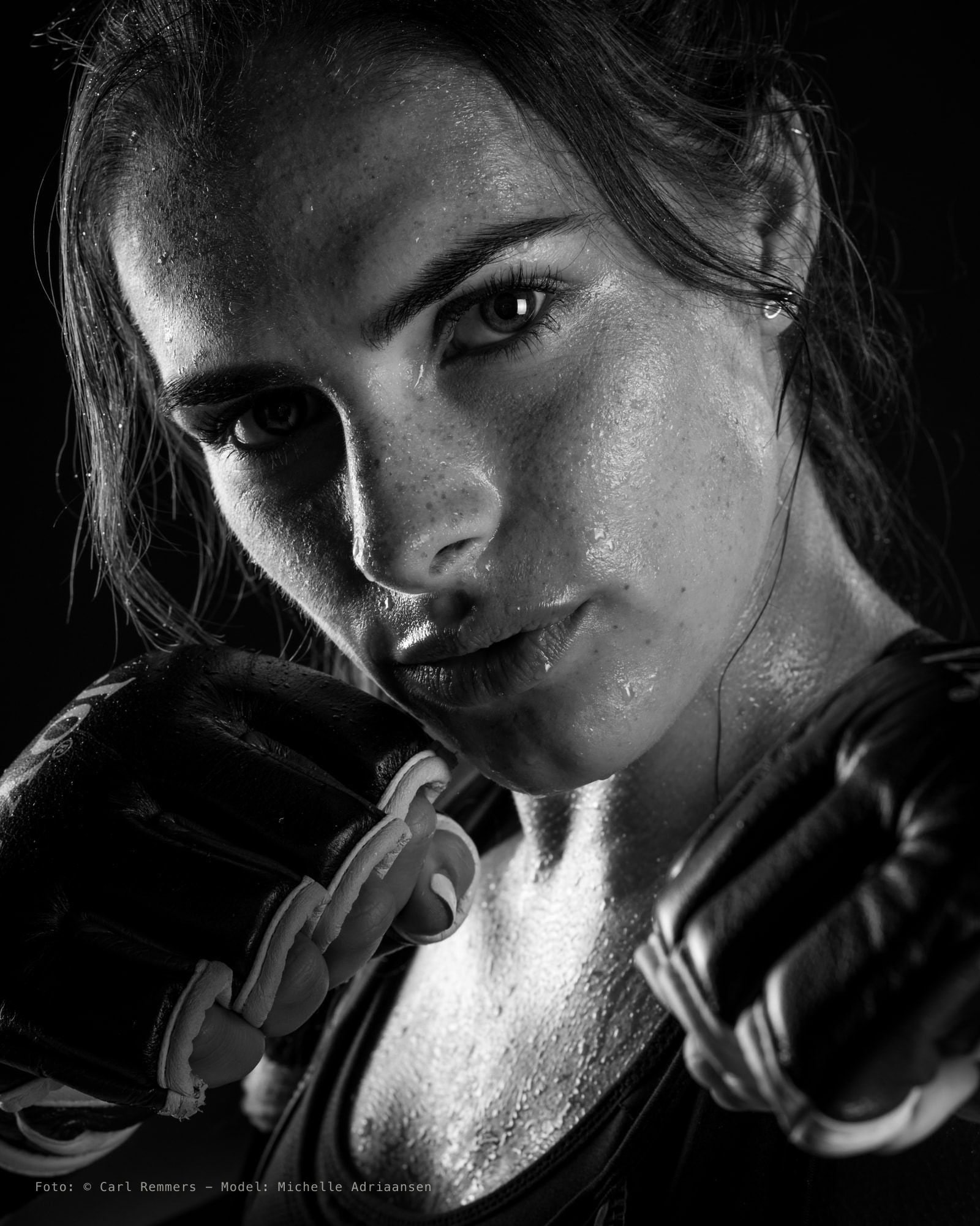 Boxer with sweat on her face and her gloves up, black and white