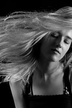 Vrouw zwiept haar blonde haar opzij met haar ogen dicht, zwart-wit