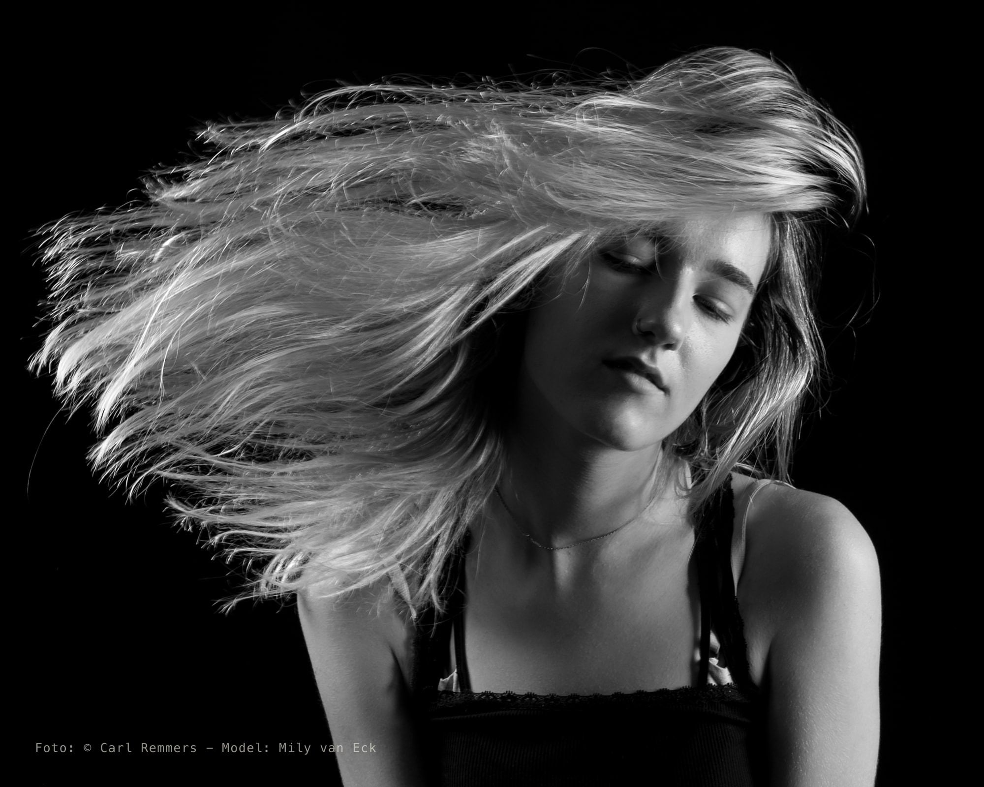 Vrouw zwiept haar blonde haar opzij met haar ogen dicht, zwart-wit