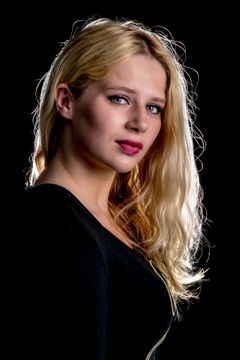 Vrouw met lang blond haar in een zwarte top, donkere achtergrond