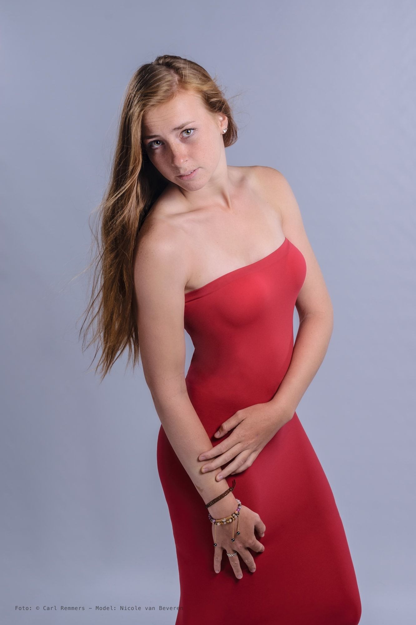Vrouw in een rode strapless jurk, lang haar over haar schouder, grijze achtergrond