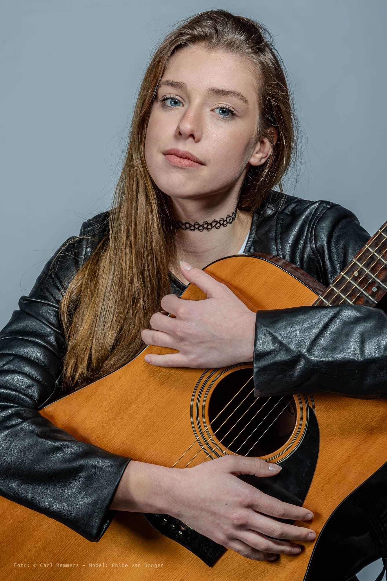 Woman with an acoustic guitar and a black leather jacket, grey background