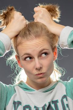 Vrouw houdt twee bosjes haar omhoog en trekt een grimas, groengrijze trui