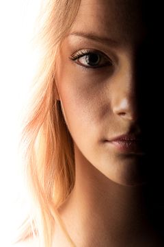 Halve gezicht van een blonde vrouw, links wit uitgelicht, rechts in schaduw.