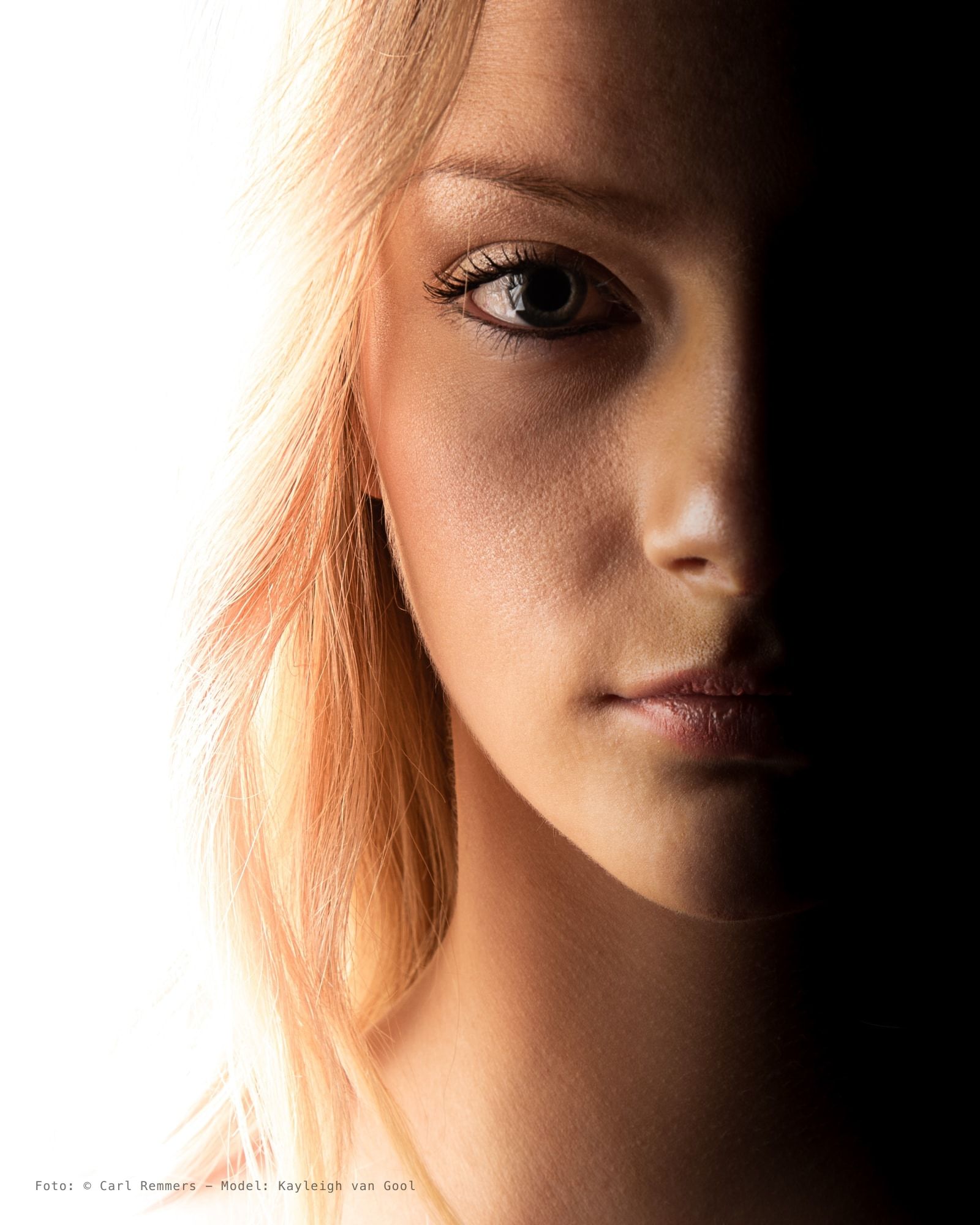 Half a blonde woman's face, lit white on the left, in shadow on the right.