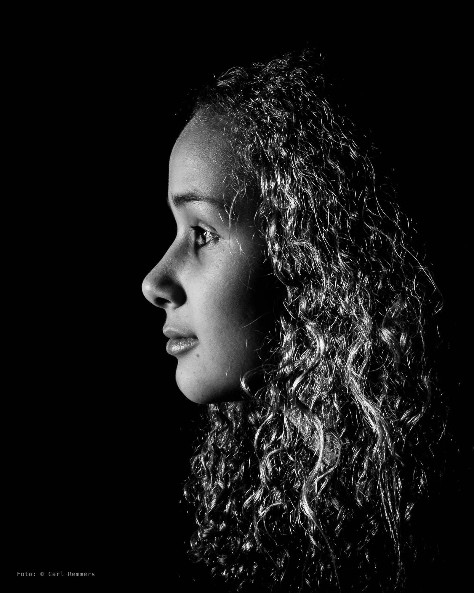 Side profile of a woman with curly hair in raking light, black background
