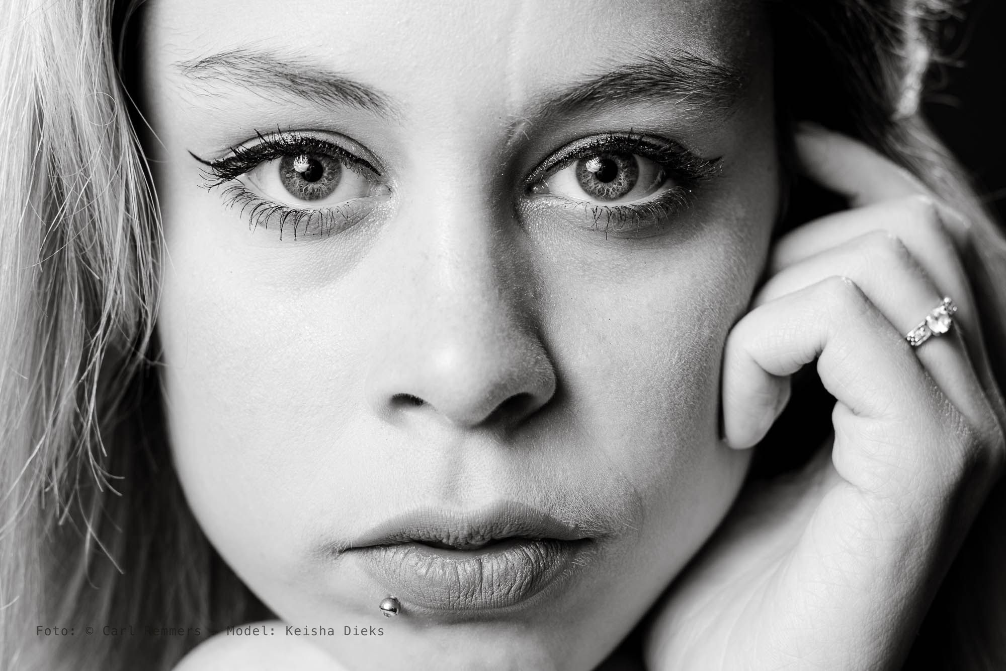Close-up met een hand tegen de wang en een piercing onder de lip, zwart-wit