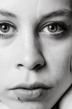 Close-up met een hand tegen de wang en een piercing onder de lip, zwart-wit