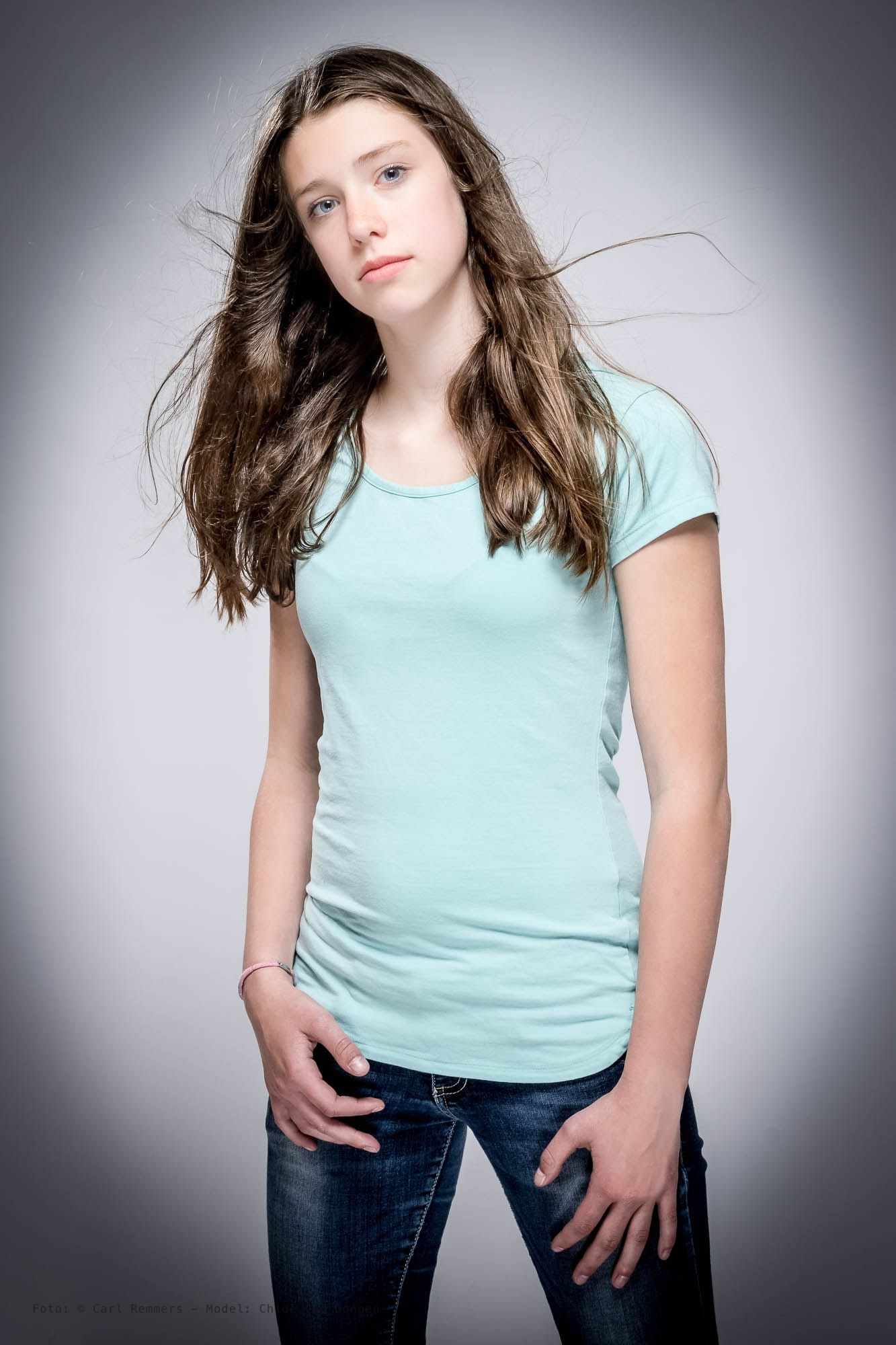 Jonge vrouw in een mintgroen T-shirt met waaiend haar, grijze achtergrond
