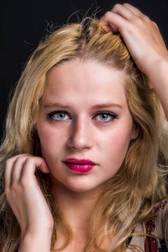 Vrouw met blond haar en roze lippen, handen in haar haar, donkere achtergrond