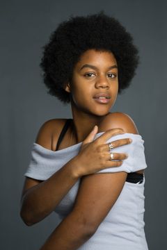 Vrouw met afrokapsel trekt een witte trui van haar schouder, grijze achtergrond