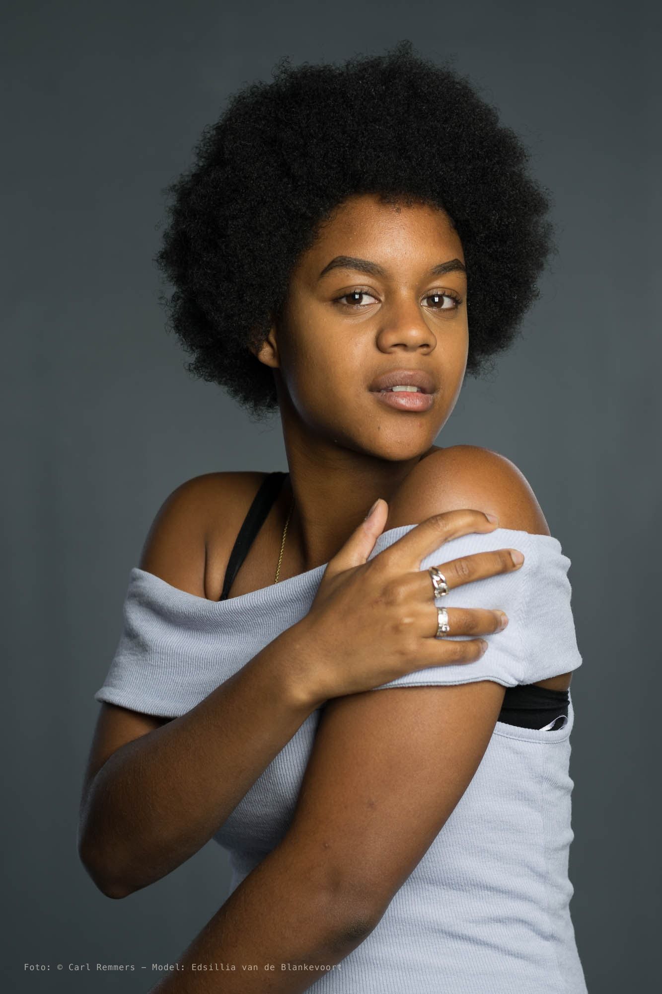 Vrouw met afrokapsel trekt een witte trui van haar schouder, grijze achtergrond