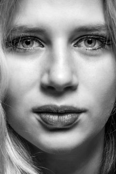 Close-up recht in de camera, blond haar langs de wangen, zwart-wit