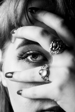 Oog achter een hand met ringen en donker gelakte nagels, zwart-wit