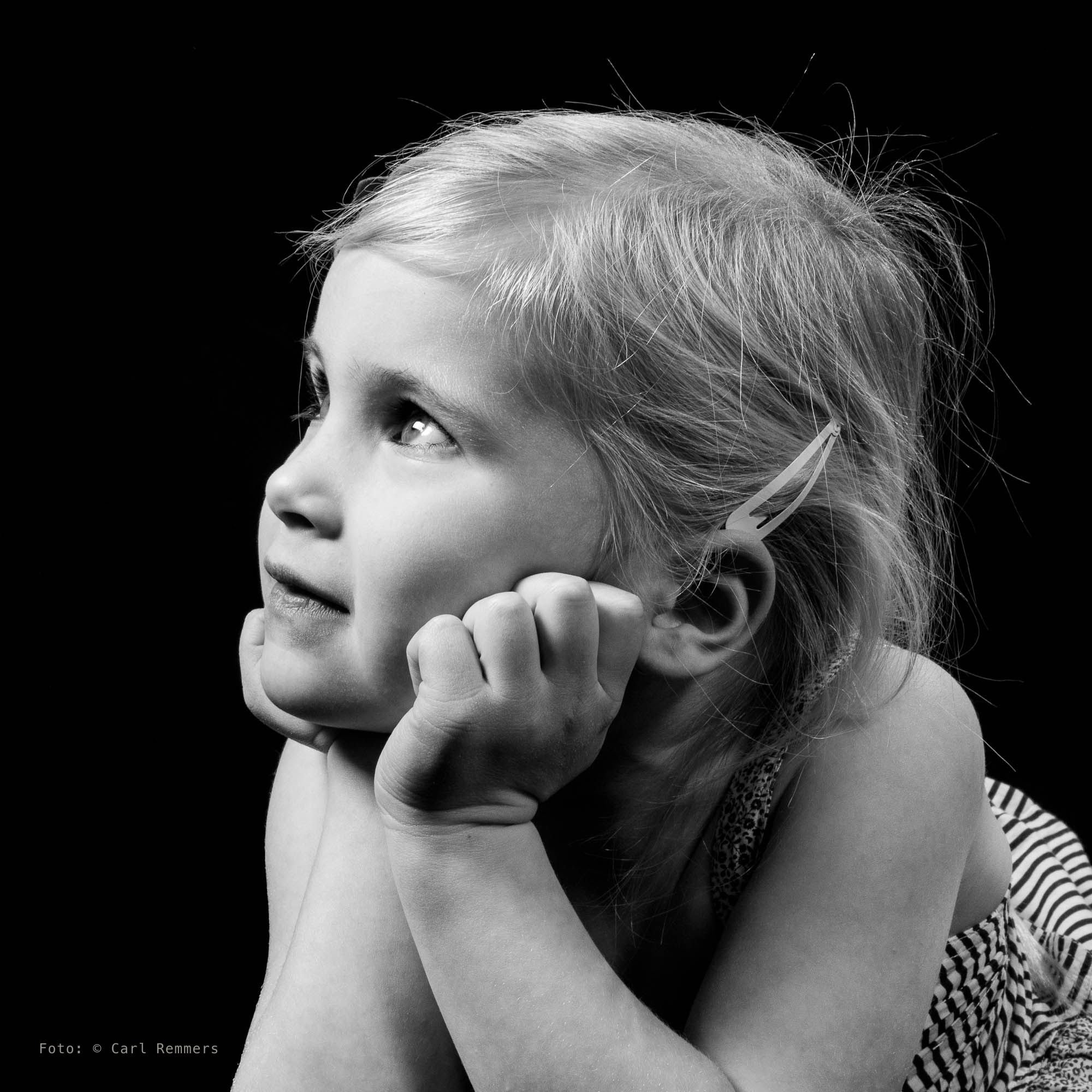 Young girl with her chin on her fist looking up, black background