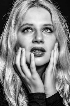 Vrouw met haar handen langs haar gezicht kijkt omhoog, zwart-wit