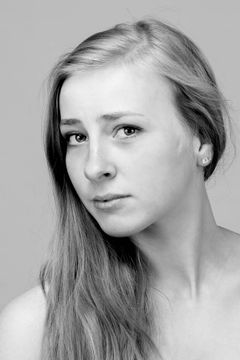 Vrouw met blote schouders en lang haar tegen een zachte grijze achtergrond, zwart-wit