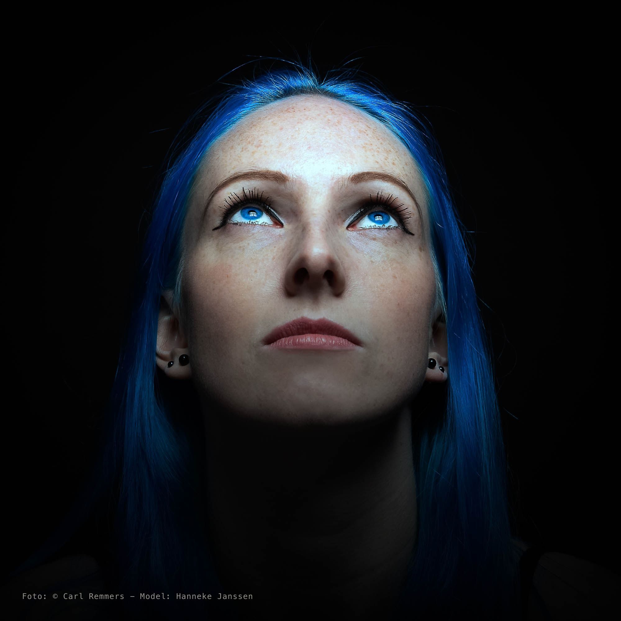 Vrouw met blauw haar en sproeten kijkt omhoog, zwarte achtergrond