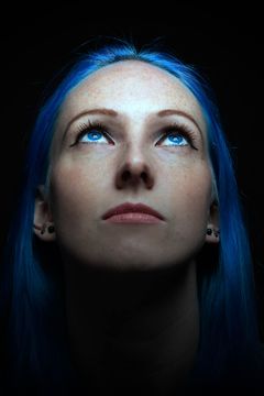 Vrouw met blauw haar en sproeten kijkt omhoog, zwarte achtergrond