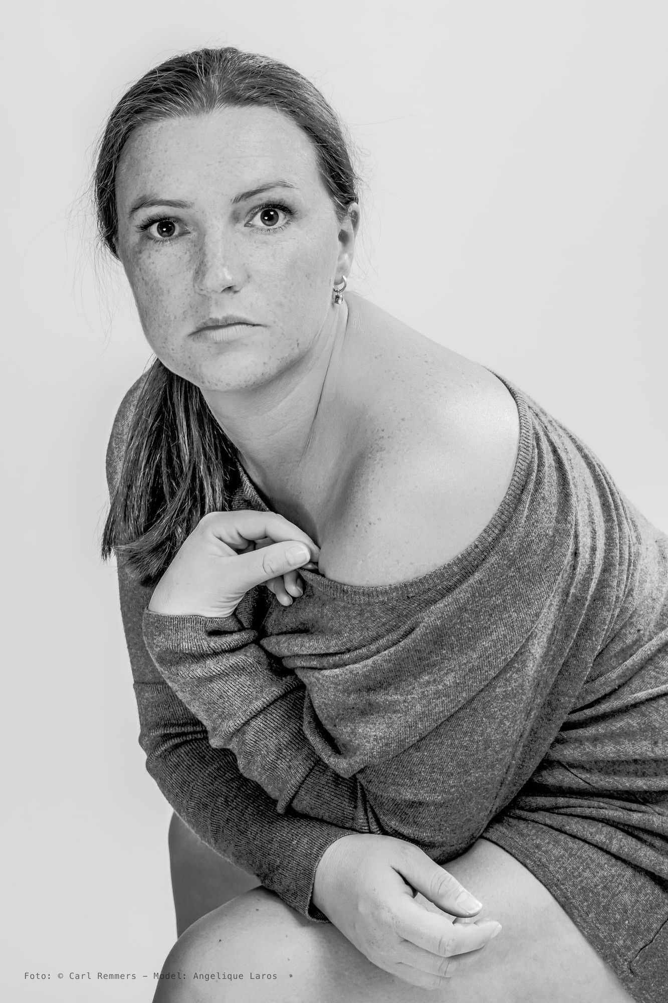 Zwart-witportret van een vrouw met sproeten in een afgezakte trui, tegen lichte achtergrond.