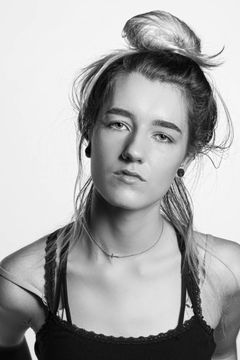 Vrouw met een hoge knot en losse lokken in een zwart hemd, witte achtergrond
