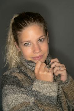 Vrouw in een dikke coltrui trekt de kraag omhoog, grijze achtergrond