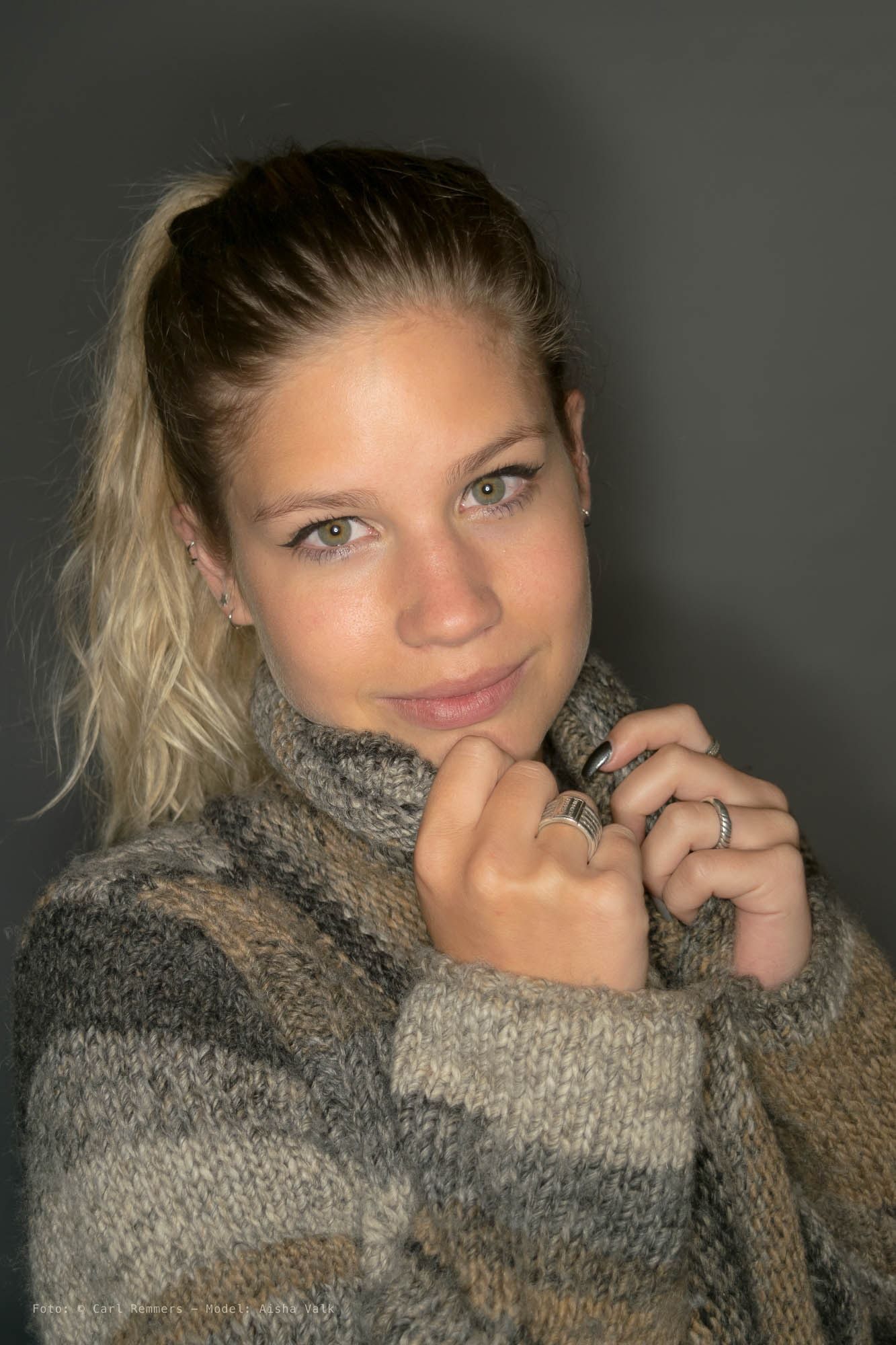 Vrouw in een dikke coltrui trekt de kraag omhoog, grijze achtergrond
