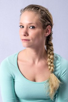 Vrouw met blonde vlecht over haar schouder in mintgroen shirt tegen lichtgrijze achtergrond.