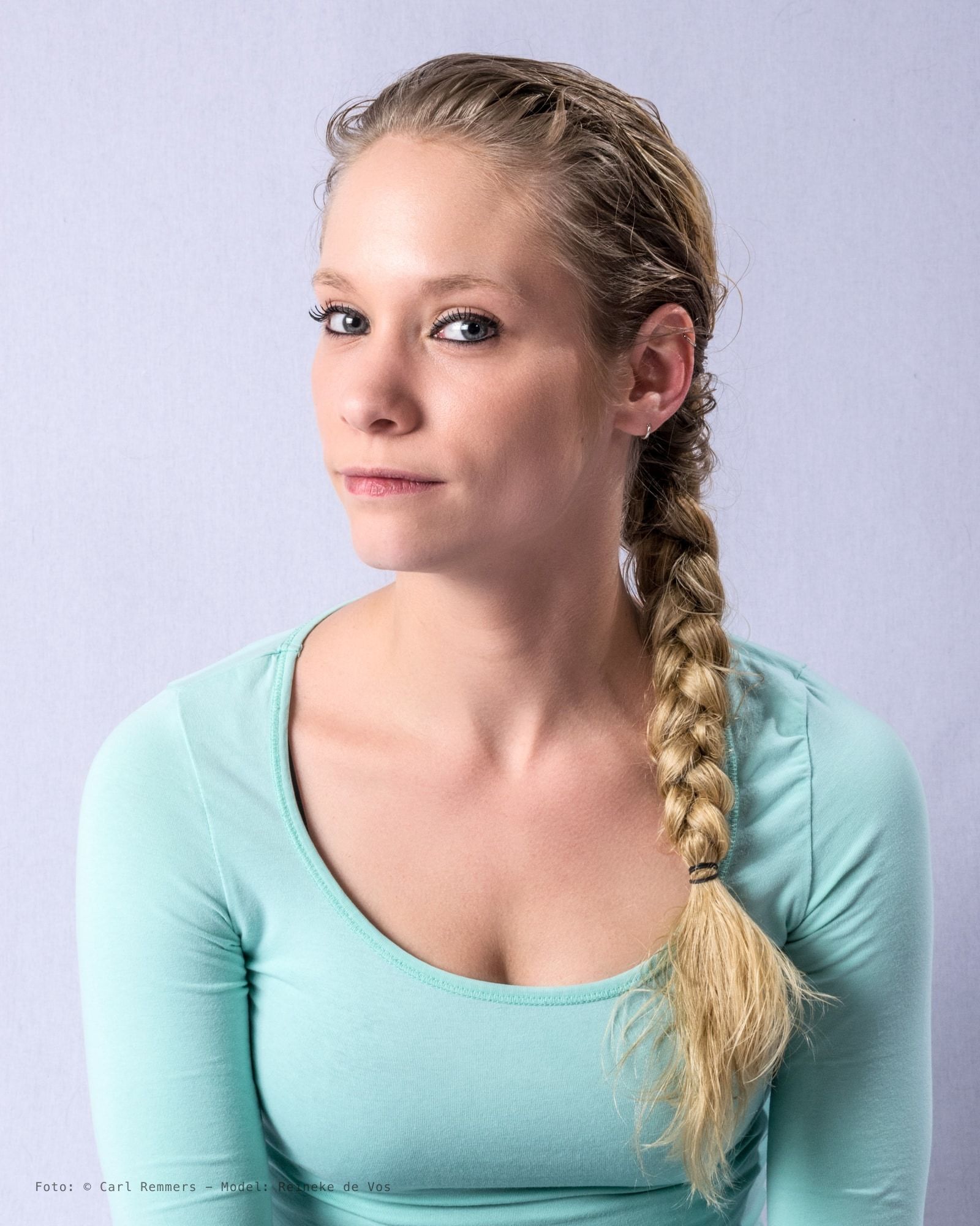 Vrouw met blonde vlecht over haar schouder in mintgroen shirt tegen lichtgrijze achtergrond.